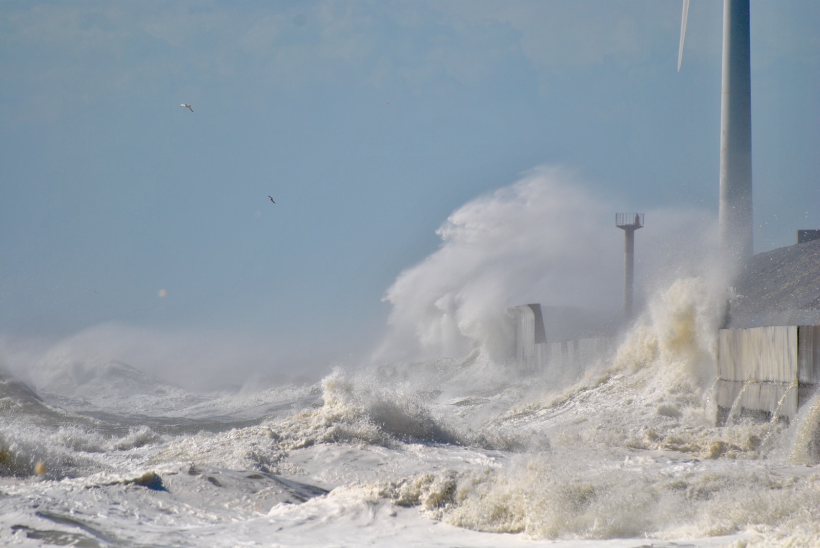 a large wave crashes against a building and wind turbines